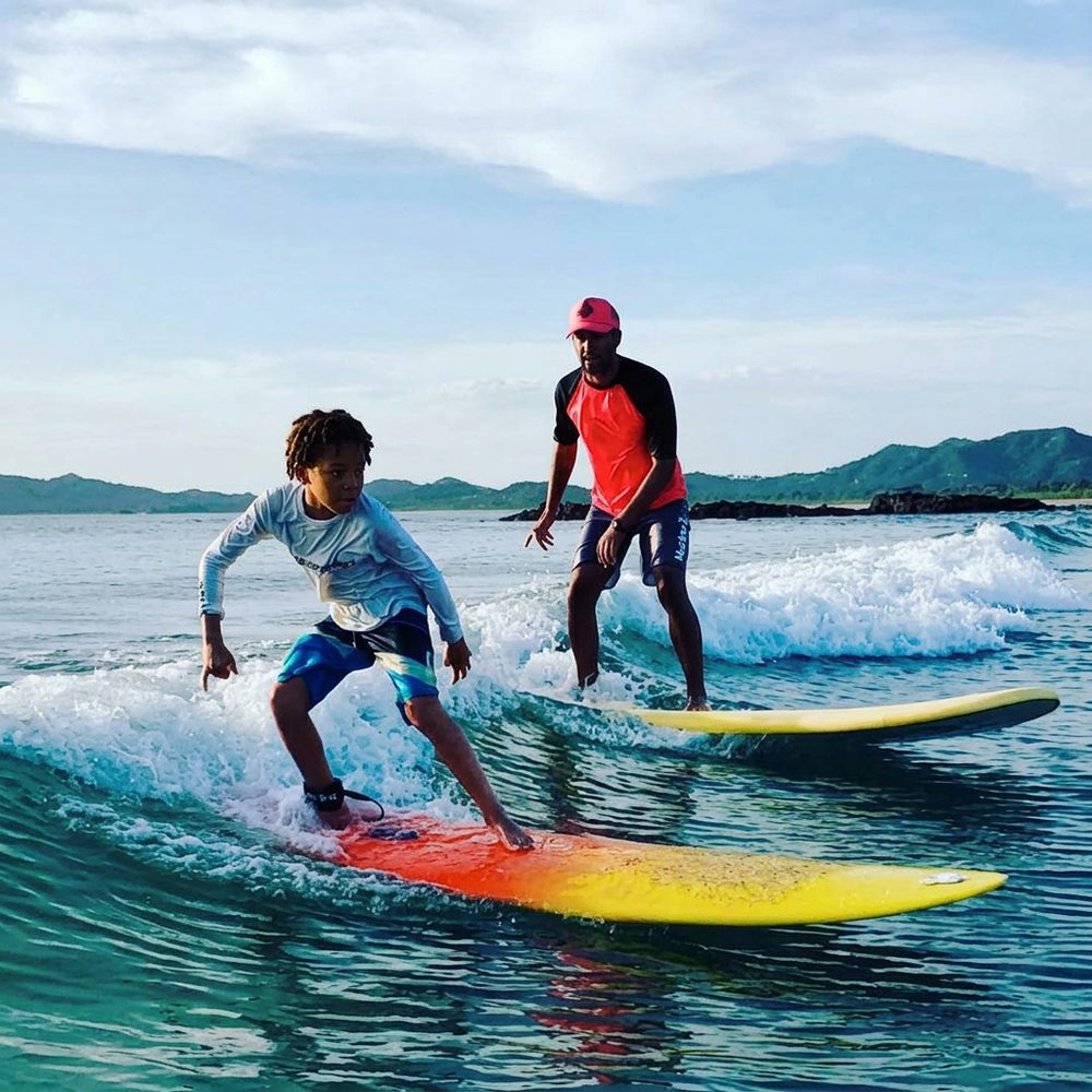 A child surfing alongside an instructor